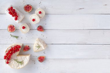 Hint peyniri ve keçi peyniri beyaz ahşap arka planda, beyaz frenk üzümü ve biberiye dilimleri ile süslenmiş, üst manzara, kopyalama alanı