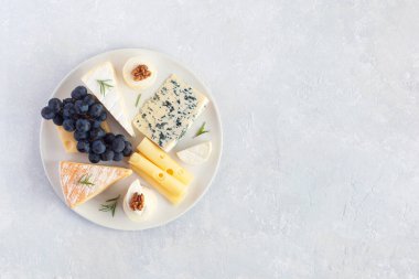 Üzüm ve cevizlerle servis edilen peynir tabağı gri beton arka planda, üst tarafta.