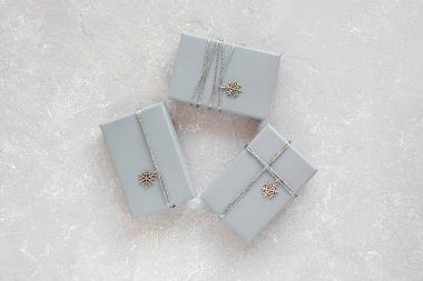 Gri çimento arka planda gümüş metal kar taneleriyle süslenmiş gri Noel hediye kutuları.