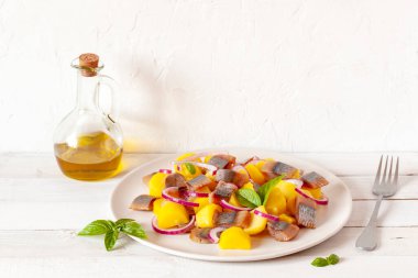 Tütsülenmiş hering, sarı patates ve kırmızı soğan salatası beyaz bir tabakta servis edilir ahşap arka planda