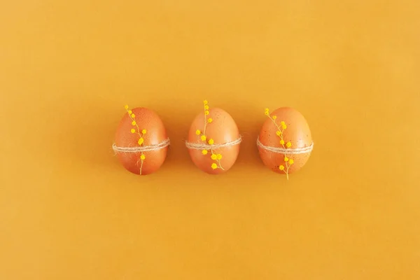Tres huevos amarillos de Pascua decorados con flores de mimosa, vista superior —  Fotos de Stock