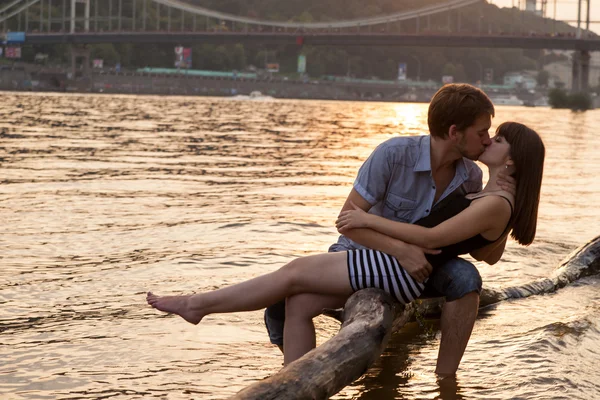 Пара обіймає і цілується на березі річки Стокове Зображення