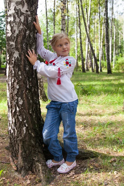 Child in Ukrainian style shirt by a birch in a forest — Stock Photo, Image