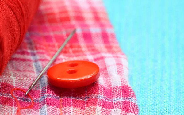 Botón rojo en un paño de algodón con aguja — Foto de Stock