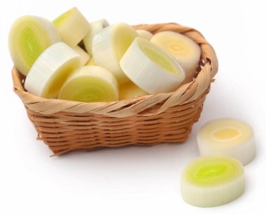 Beyaz arka planda sepetin içinde taze pırasa parçaları.