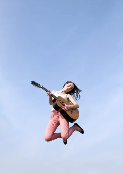 Mujer saltando con la guitarra en el cielo azul — Foto de Stock