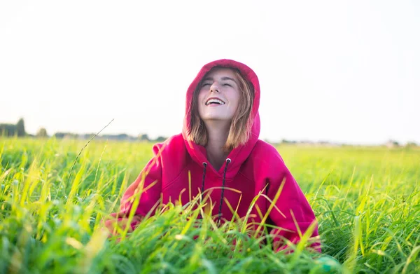 幸せな若い女の子は夕方の太陽の下で牧草地に座って — ストック写真