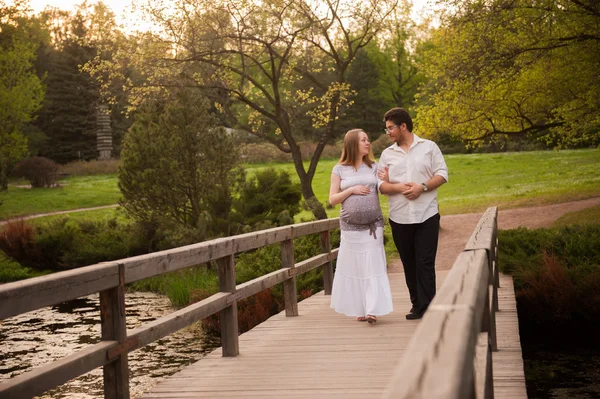 A man with a pregnant woman on the bridge in the park — Stock Photo, Image