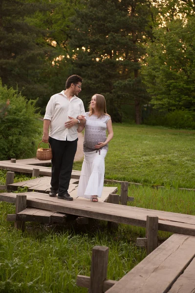 A man with a pregnant woman on the bridge in the park — Stock Photo, Image