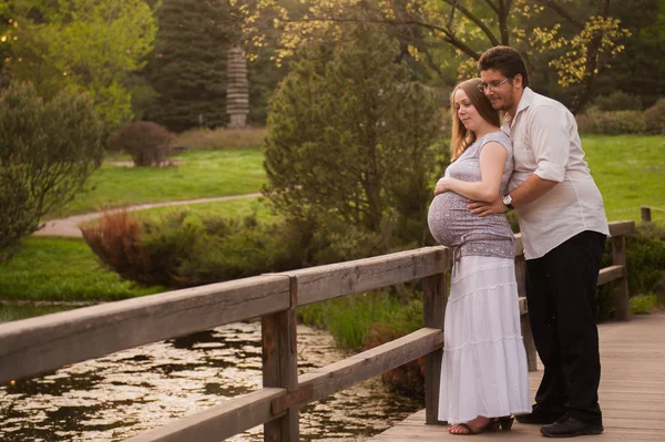 Um homem com uma mulher grávida na ponte do parque — Fotografia de Stock