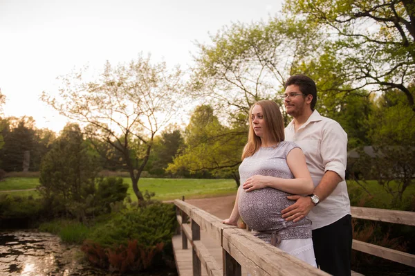 Um homem com uma mulher grávida na ponte do parque — Fotografia de Stock