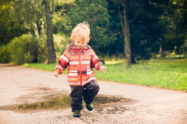 Niño corriendo y saltando en charcos — Foto de Stock