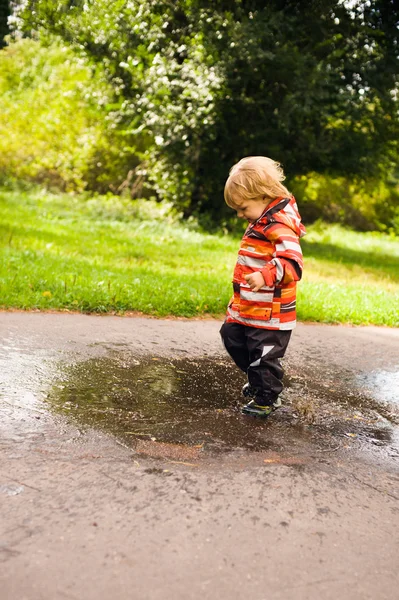 Pojken springa och hoppa i vattenpölar — Stockfoto