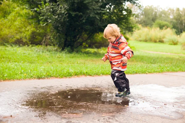 Niño corriendo y saltando en charcos — Foto de Stock