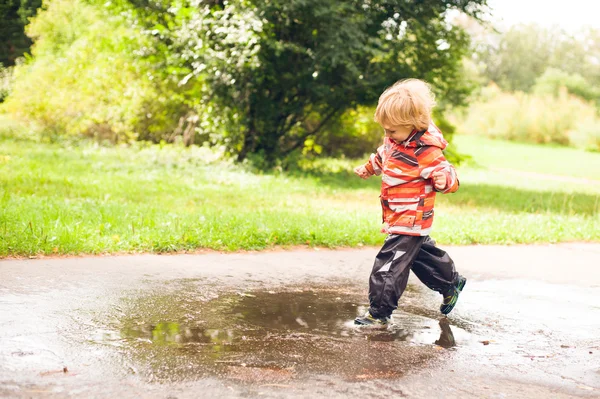 Menino correndo e pulando em poças — Fotografia de Stock