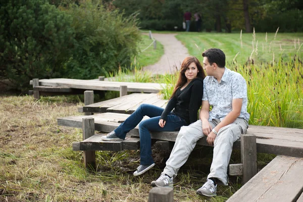 Ζευγάρι στην αγάπη που κάθεται στη γέφυρα στο πάρκο φθινόπωρο — Φωτογραφία Αρχείου