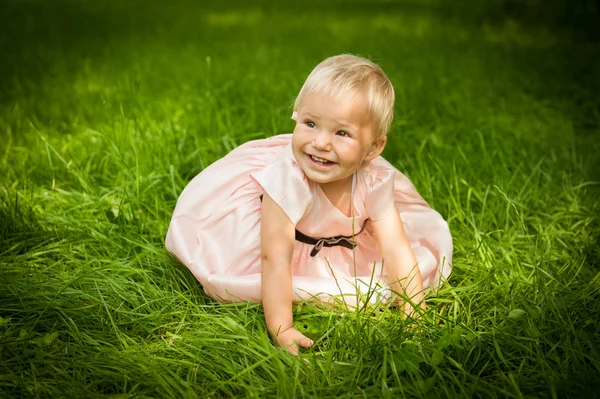 Menina bonito está sentado na grama e sorrindo — Fotografia de Stock