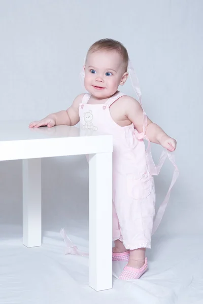 Petite fille mignonne debout, appuyée sur une table — Photo