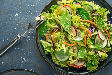 Mavi masa arkasında taze karışık sebzeli yeşil marul salatası.