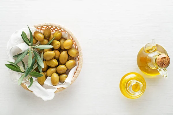 Olive oil bottle and olives with branch in basket on wooden table