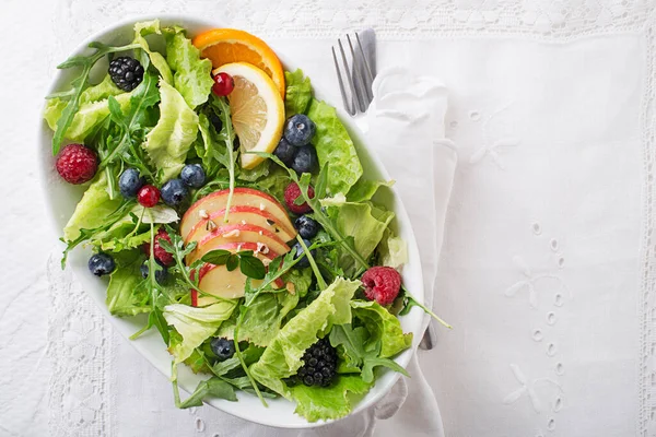Healthy green salad with berry and apple fruit on white background. Fresh salad with fruits and greens. Healthy food.