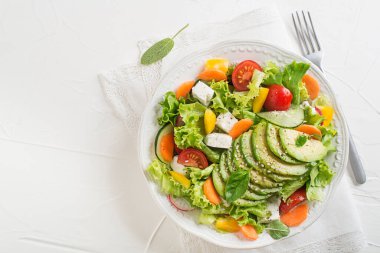 Avokado, peynir ve beyaz arka planda taze sebzeli sağlıklı yeşil salata.