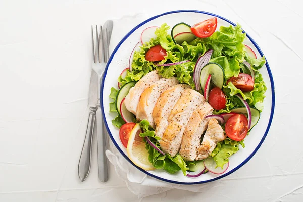 Healthy green salad with chicken breast and fresh vegetables on white table close up