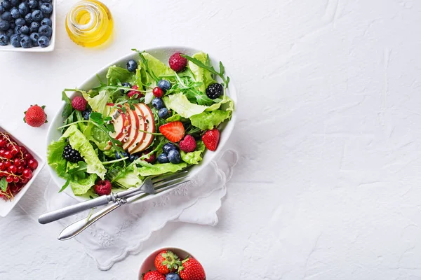 Healthy green salad with berry and apple fruit on white background. Fresh salad with fruit ingredients and greens. Healthy food.