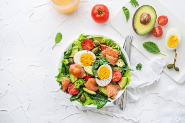 Fresh green salad with smoked salmon, cherry tomatoes, egg and avocado on white table background