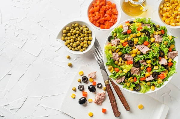 Healthy Green salad with tuna, corn, carrots, peas, and olives on white table background. Mexican corn salad.