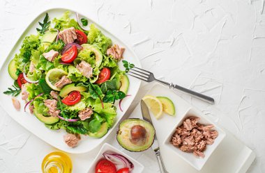 Fresh green leafy salad with tuna avocado and tomato on white table background. Concept for a tasty and healthy meal
