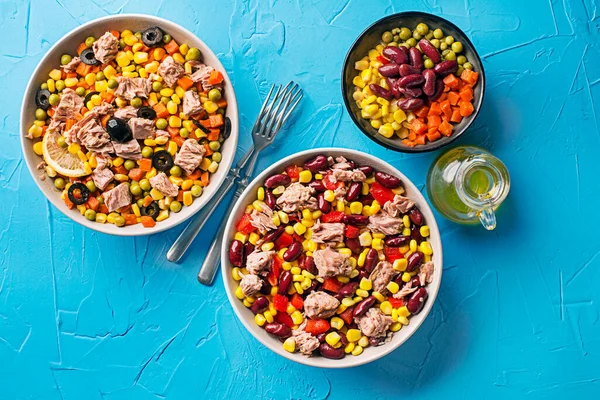 Healthy mixed tuna salads with corns, carrots, peas, beans, peppers and olives on blue table background. Mexican corn salad.