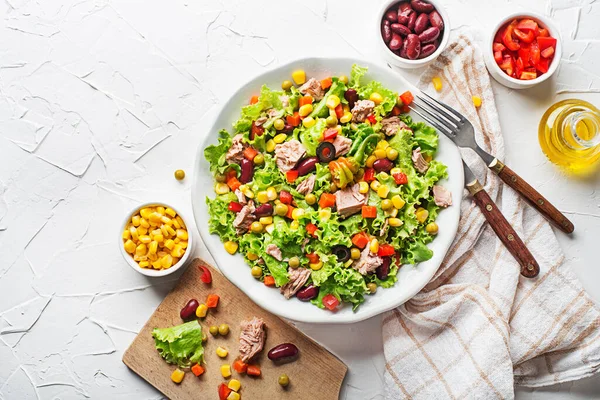 Healthy Green salad with tuna, corn, carrots, peas, pepper, beans and olives on white table background. Mexican corn salad.
