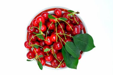 Kırmızı, lezzetli, olgun kirazlı bir tabak ve beyaz arka planda yapraklı bir filiz.