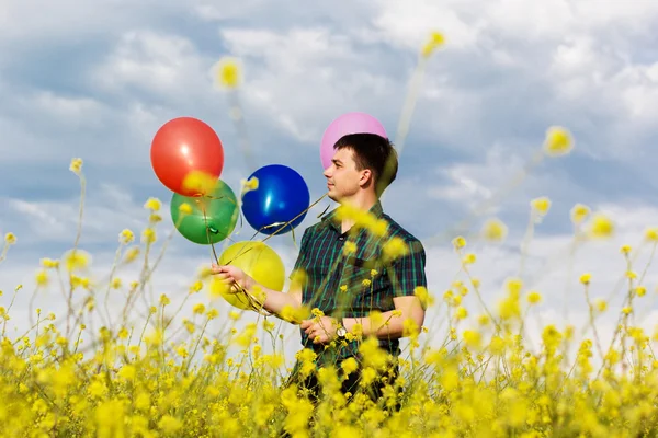 Jonge man in een veld van de lente met veel ballonnen — Stockfoto