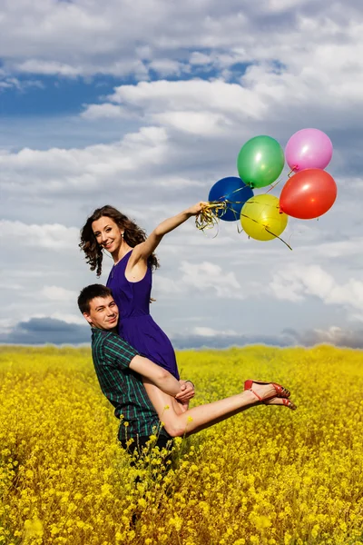 Happy couple with balloons on the yellow field — Stock Photo, Image