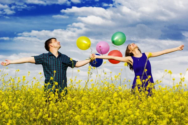Pareja feliz con globos en el campo amarillo — Foto de Stock