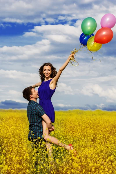Casal feliz com balões no campo amarelo — Fotografia de Stock