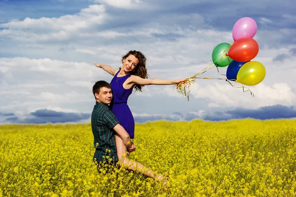 Glückliches Paar mit Luftballons auf dem gelben Feld — Stockfoto