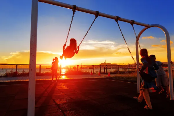 Criança jogando swing contra o pôr do sol — Fotografia de Stock