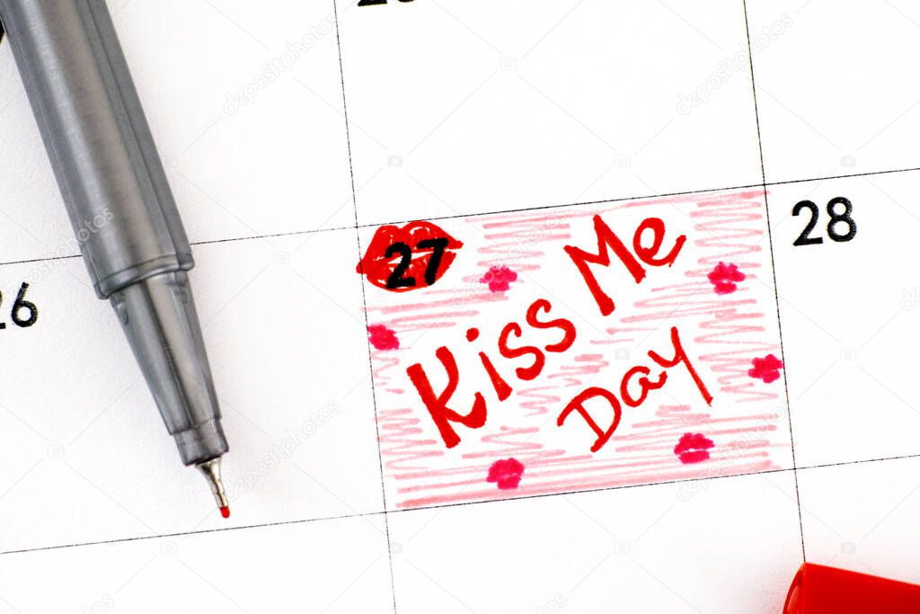 Handwriting reminder Kiss Me Day in calendar with pen. August 27