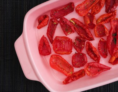 Siyah peçeteli, güneşte kurutulmuş domatesli pembe fırın tabağı. Üst görünüm. 
