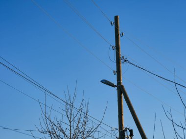Elektrik hatları ve mavi gökyüzüne karşı tahta bir direkte lamba..