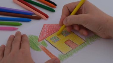 Sarı balmumu pastel boyalı bir evi boyayan bir kadın..