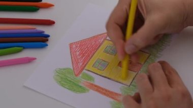 Sarı balmumu pastel boyalı bir evi boyayan bir kadın..