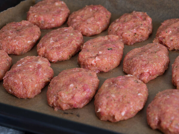 Raw meat cutlets in a backing tray are ready to be cooked