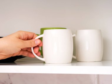 Mutfak rafından beyaz kupa alan bir kadın..