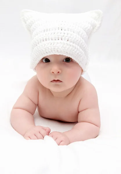 Beautiful baby in white hat lies on bed — Stock Photo, Image