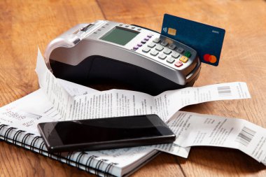 Mallar ve hizmetler için nakit olmayan ödemeler için POS terminalinde bir banka kartı. Masanın üzerinde banka kartı, kağıt kontrolü, not defteri ve cep telefonu olan bir POS terminali var..