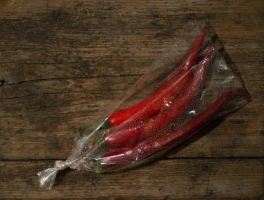 Ahşap bir arka planda plastik bir pakette kırmızı biber. Üç büyük biber..